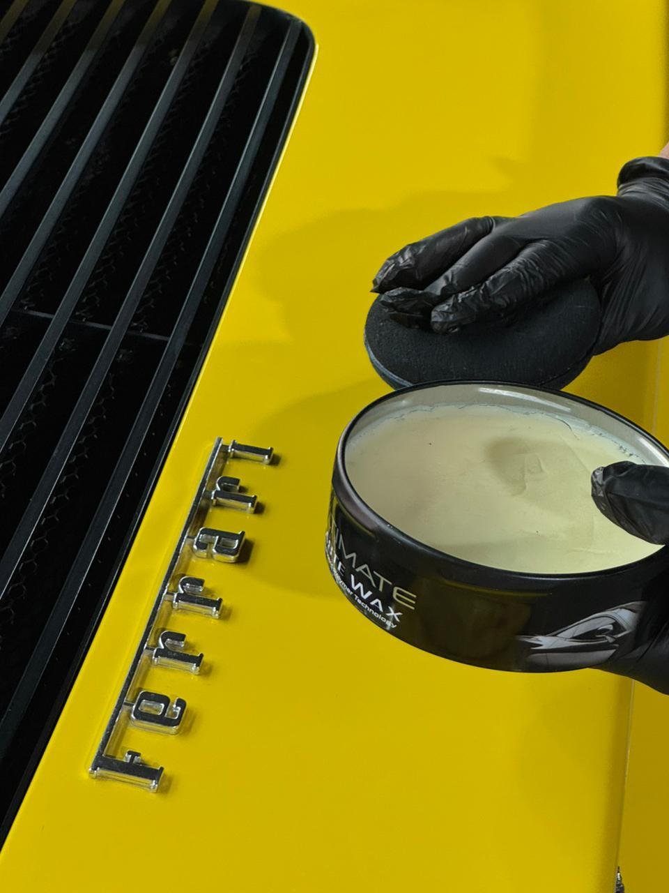 Emblema Ferrari y cera Meguiar’s Ultimate Paste Wax sobre el capó amarillo